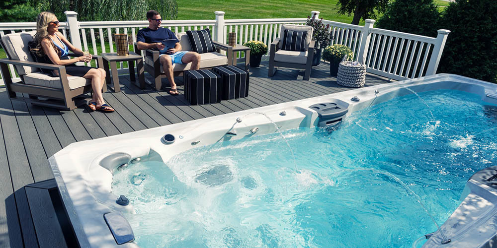 Een stel dat op hun terras zit te ontspannen naast een zwemspa waarvan de waterpartijen aan staan.