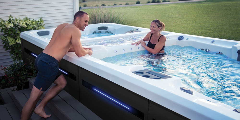 Een man die over de rand van een H2X-zwemspa leunt om een gesprek te voeren met een vrouw die van het water geniet.